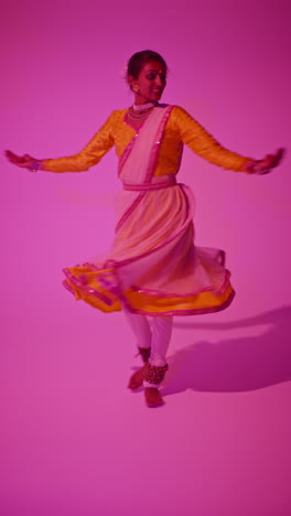 vertical video full length studio shot of female kathak dancer performing dance wearing traditional indian dress against purple background 6