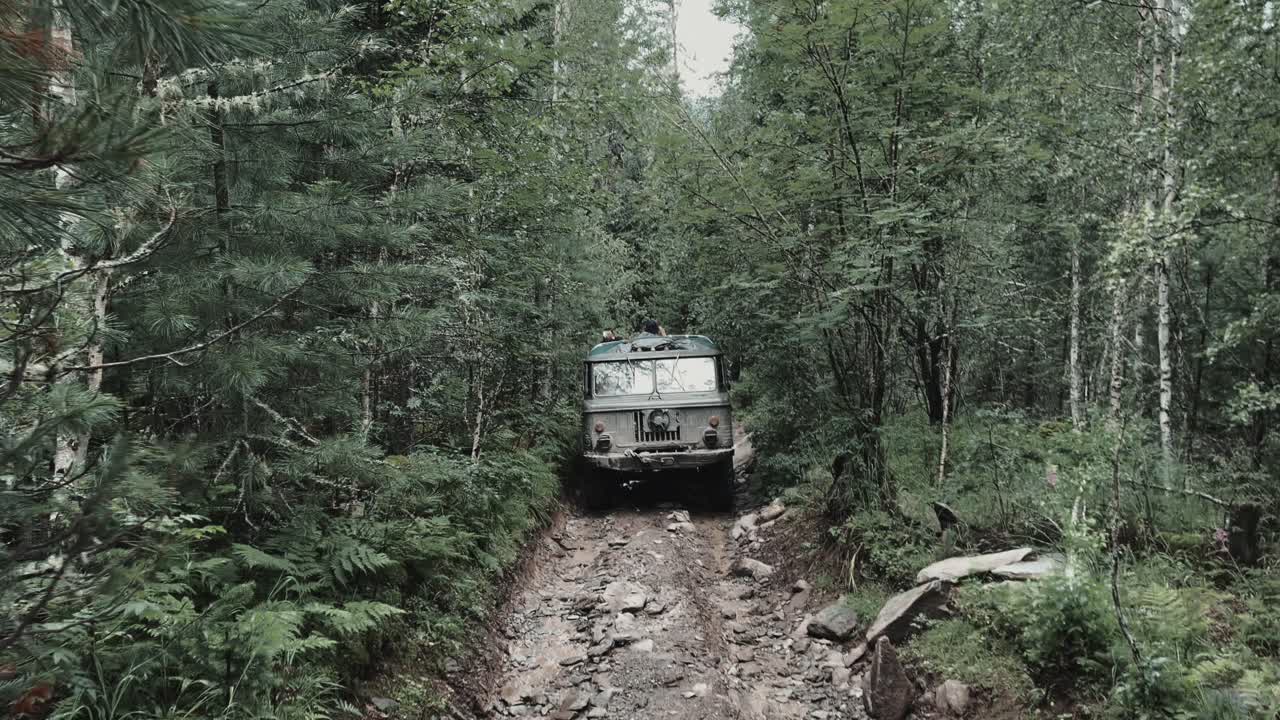 Un robusto fuoristrada 4x4 percorre una strada sterrata rocciosa attraverso una fitta foresta di conifere sui Monti Altai, Repubblica dell'Altai, Russia, viaggio in luoghi selvaggi e remoti.