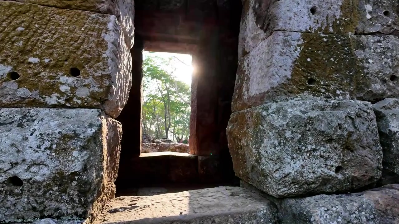 Raggi di sole dorati che filtrano attraverso le finestre di pietra delle antiche rovine Khmer, Parco Storico di Phanom Rung, Buri Ram, Thailandia