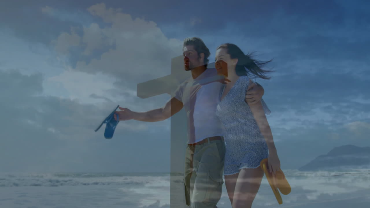 Walking on beach, couple holding cross with ocean waves in background