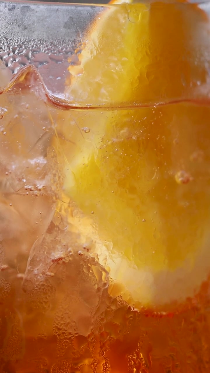 Close-up of a chilled Aperol Spritz with lemon slice, highlighting condensation and vibrant colors in soft lighting