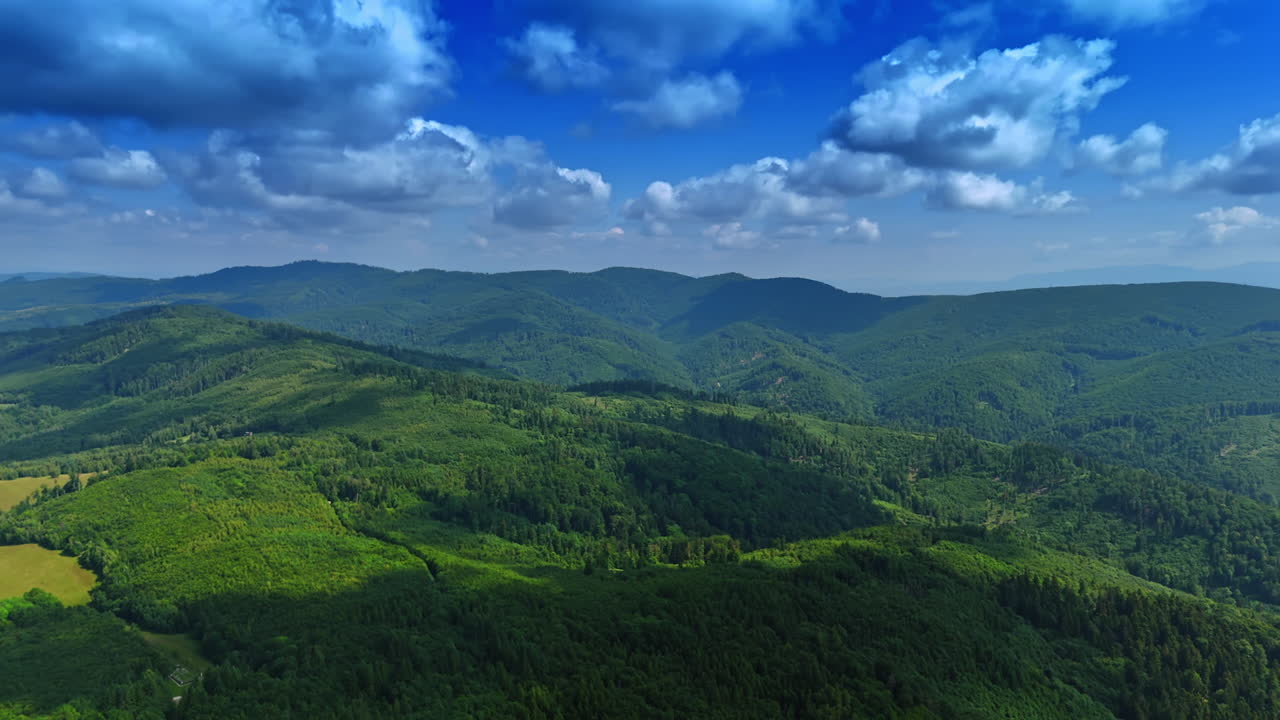 Lush green hills under a blue sky. Expansive green hills and valleys stretch under a bright blue sky with fluffy clouds in the distance