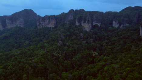 limestone cliffs and lush tropical jungle of railay beach, krabi, thailand, at dusk, creating a dramatic and serene landscape. dramatic aerial view flight fly reverse drone