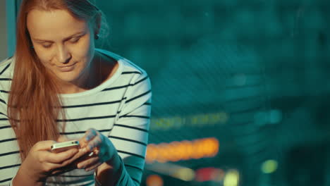 Mujer-Usando-El-Teléfono-Sentada-Junto-A-La-Ventana-Por-La-Noche