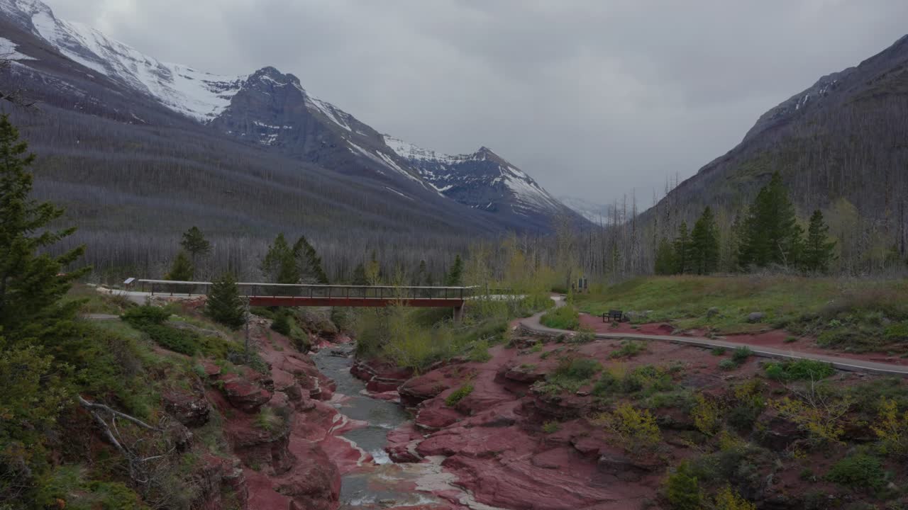 Rivière du canyon Rouge coulant à travers des formations rocheuses rouges avec un pont et des montagnes dans le parc national des Lacs-Waterton