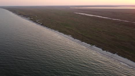 Astonishing-aerial-revealing-shot-of-the-wild-beaches-of-Vadu,-Romania-where-the-Black-Sea-meets-the-shore,-at-sunset