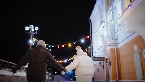 couple walking hand-in-hand in snowy city at night
