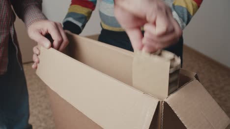 the father takes the package out of the box and then a piece of furniture to assemble. close-up on the hands with the goods. saving the family budget