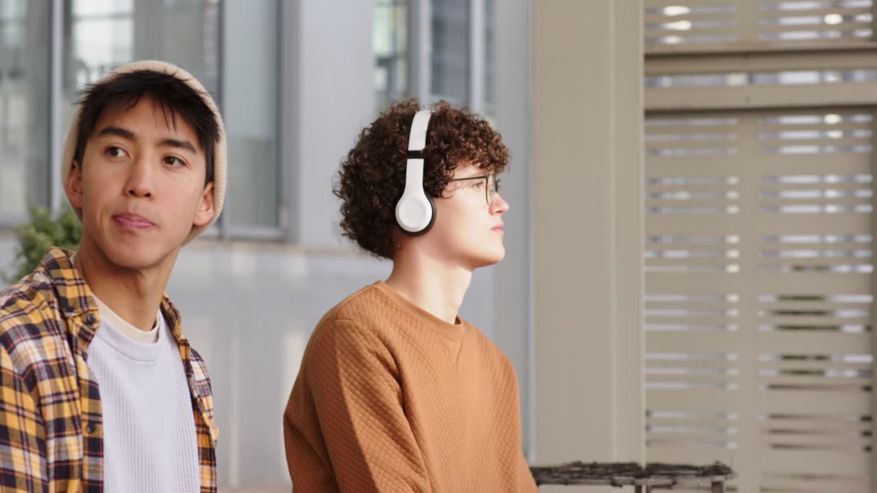 Spotting motion behind them Diverse friends wearing beanie headset leaning glancing on lobby bench