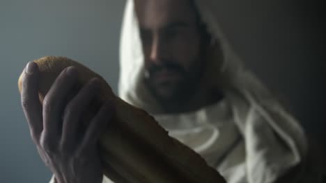 closeup of jesus christ in white hooded robe holding bread as he stands in glowing, bright light. perfect for representation of jesus as the bread of life, last supper, communion christian sacraments.