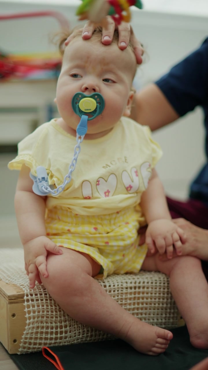 Baby engaging in a physical therapy session, receiving assistance with a pacifier from a therapist for developmental support
