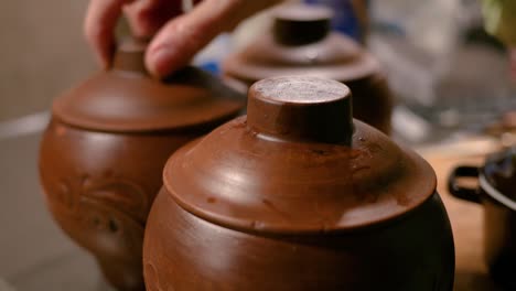 a female hand lids clay pots with vegetables to bake in the oven