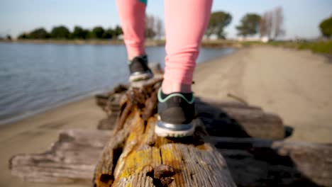 young girl walks on dead wood log like a balance beam near lake water
