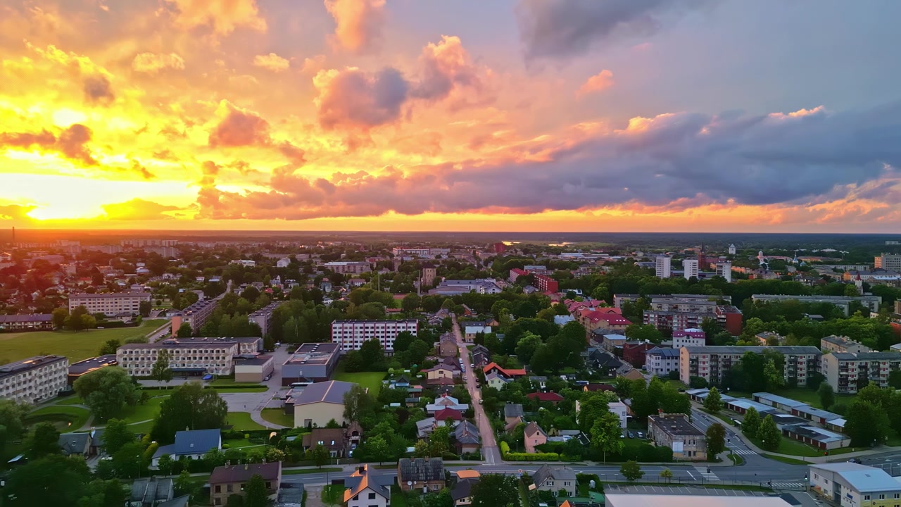 Colorful evening sky glows above a mid-sized residential town as a drone glides over tree-lined streets and apartment blocks.
