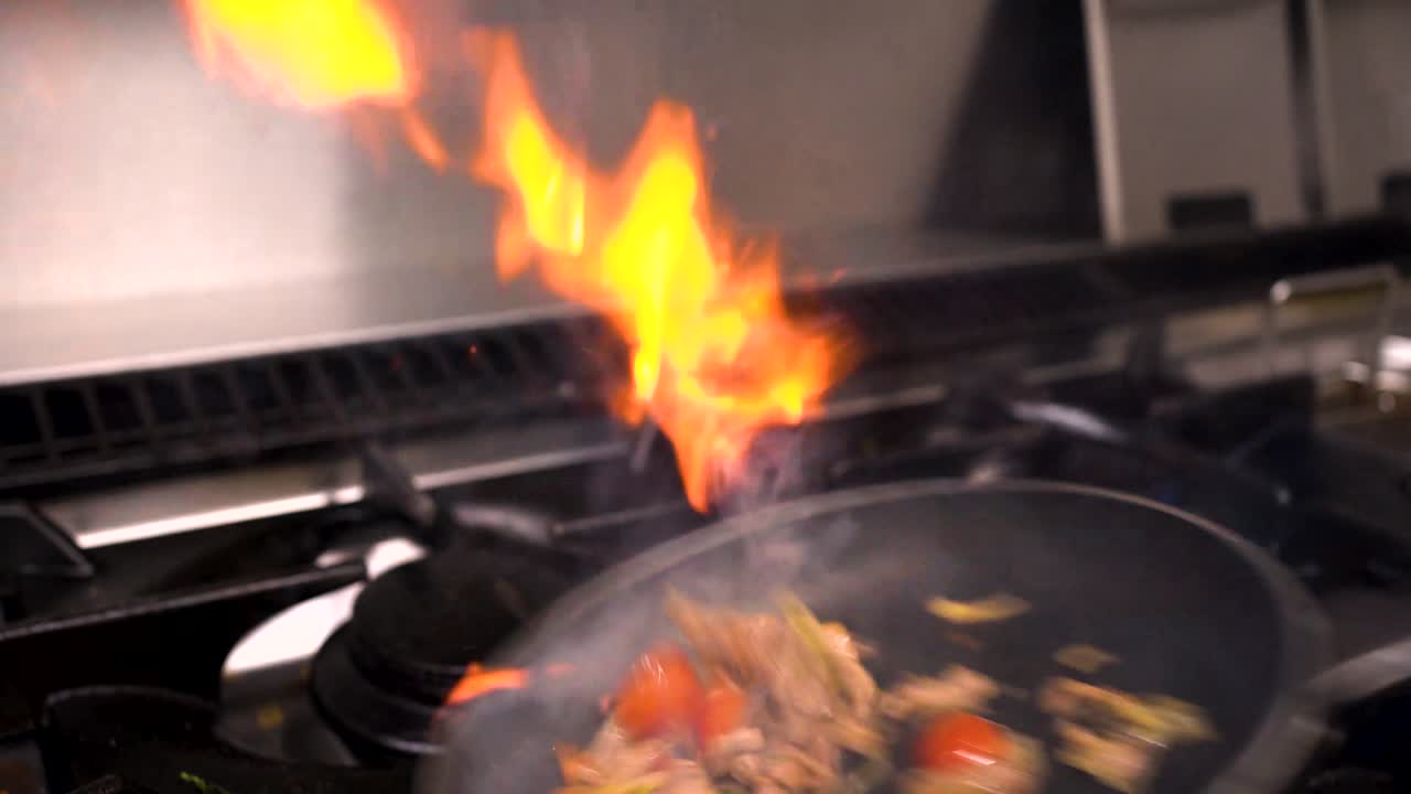 Food getting cooked in the kitchen with a nice flame show while flipping the pan.