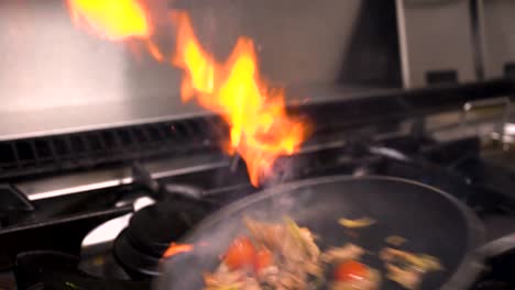 food getting cooked in the kitchen with a nice flame show while flipping the pan.