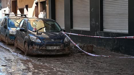 cars parked on a flooded urban street, covered with mud, indicating flood damage in valencia. the scene reflects climate change impacts