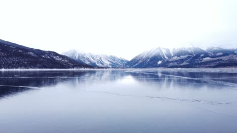 Flying-over-the-surface-of-a-frozen-lake-with-cracks-during-the-winter,-aerial