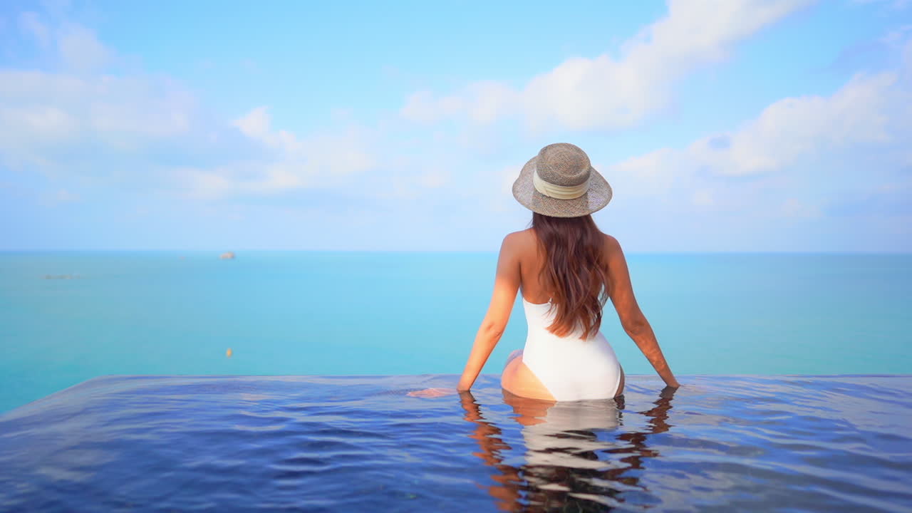Schöne Frau sitzt am Rand eines Infinity-Pools mit Blick auf das Meer.