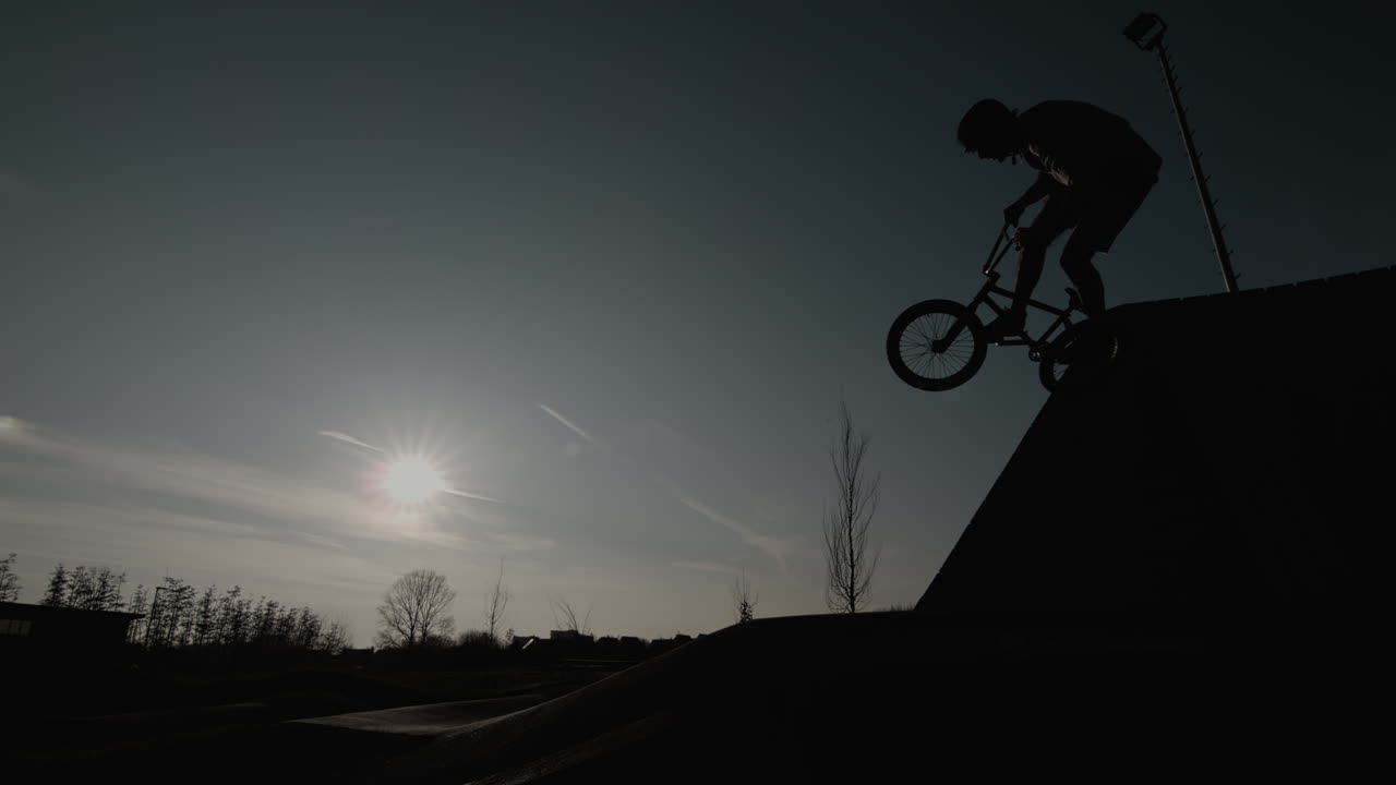 Silhouetted BMX rider performing a trick on a ramp at sunset in Goes, Netherlands, super slow motion