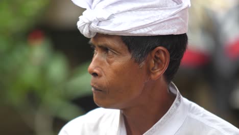 Hombre-Balinés-De-Piel-Marrón-Vestido-De-Blanco-Exhala-Humo-Por-La-Nariz,-Luego-Levanta-El-Cigarrillo-A-Los-Labios-E-Inhala