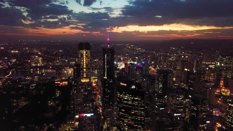 fast moving orbiting aerial view of a modern city with tall buildings, lights and dramatic clouds in the evening