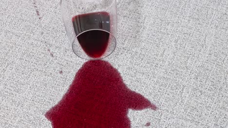 camera pans above wine glass tipped onto pale upholstery, liquid pooling