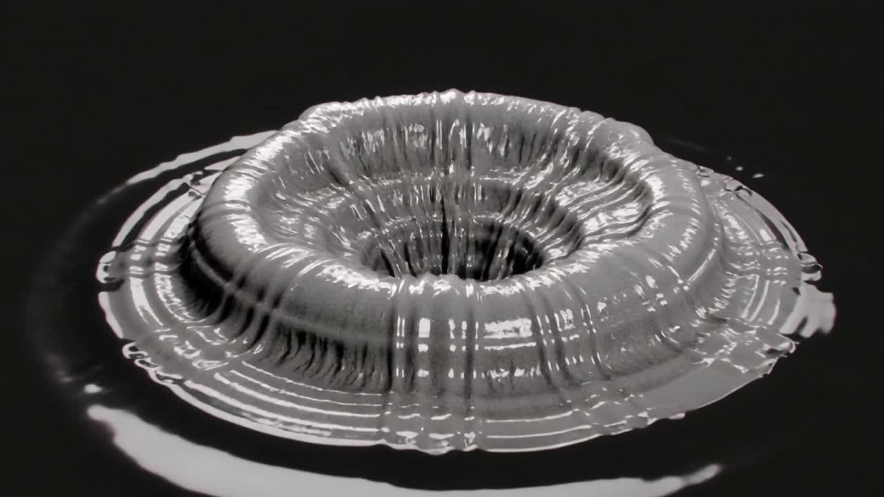 Rising metallic gray mass peaking then collapsing into torus on reflective black plane, rippling