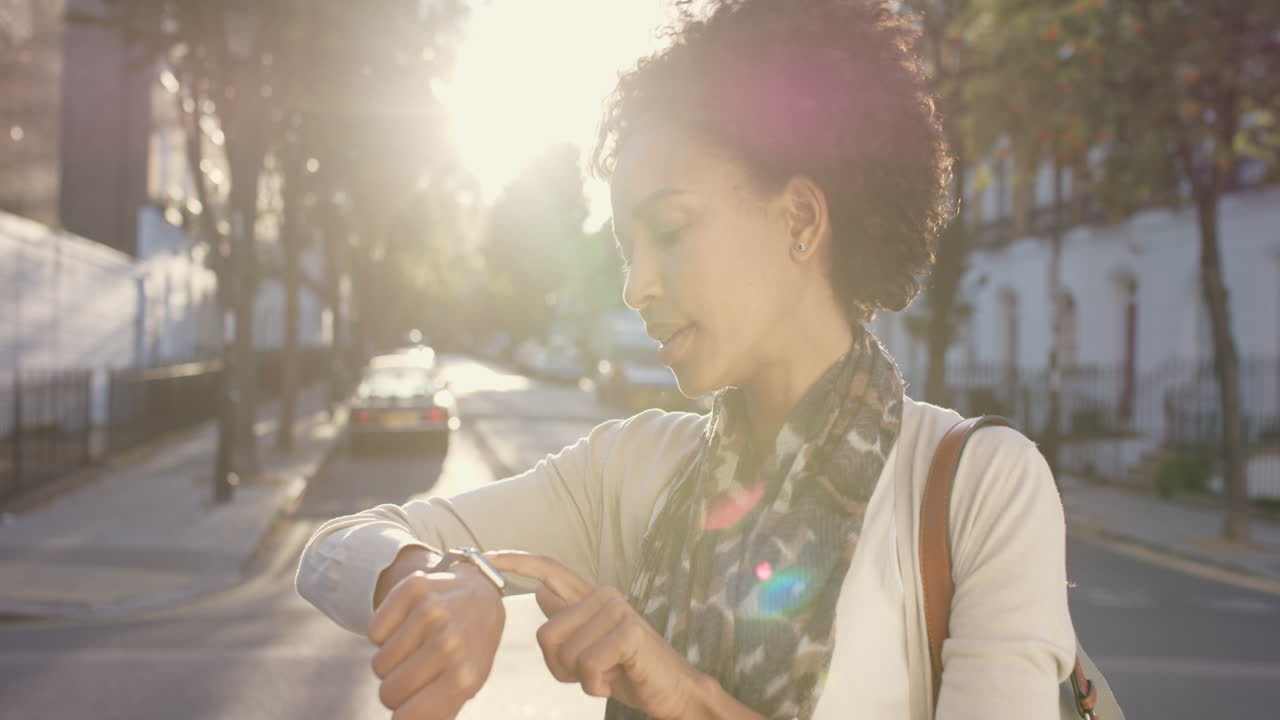 Beautiful Mixed race woman using smart watch technology walking through city