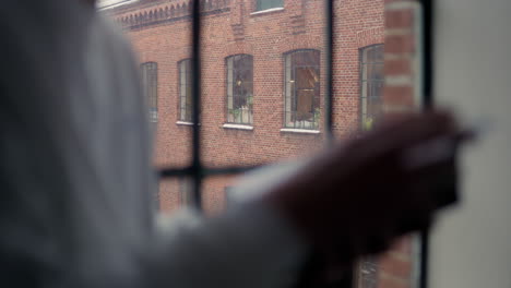 Person-engrossed-in-book-by-window-on-snowy-day