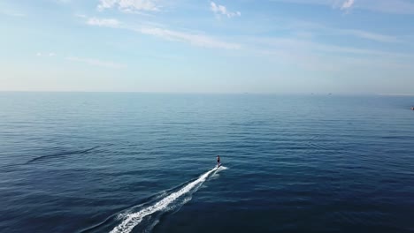 surfer riding a fast electric surfboard into the open sea on a calm sunny day, aerial follow