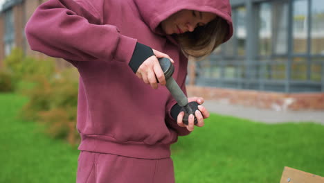 work out participant in wine hoodie tightens dumbbell end beside brick building, head bent focused during street workout, showcasing fitness dedication, perseverance, strength improvement mission