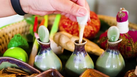 a hand carefully pours oil into small ceramic bottles surrounded by natural ingredients.
