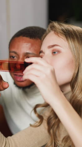 concentrated young white woman with black colleague chooses shots to print on coloured photo-film strip sitting on sofa at home slow motion