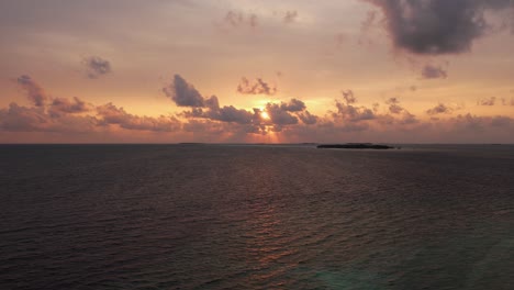 drone view of maldives sunset over calm ocean, panoramic sky and island