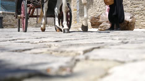 low angle view of a horse drawn carriage passing two woman on a cobblestone road