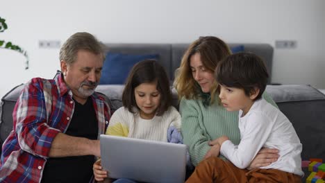 Grandfather-with-two-grandchildren-and-daughter-making-video-call,-using-laptop