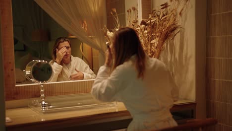 a female sitting at a beauty vanity table checking her hair and skincare in the mirror