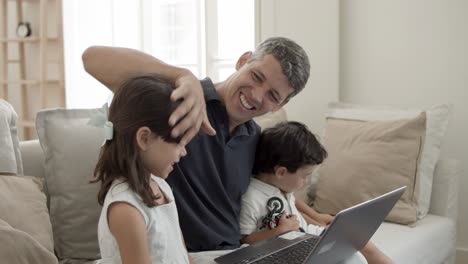 Papá-Alegre-Y-Dos-Niños-Lindos-Sentados-Frente-A-Una-Computadora-Portátil-En-La-Sala-De-Estar