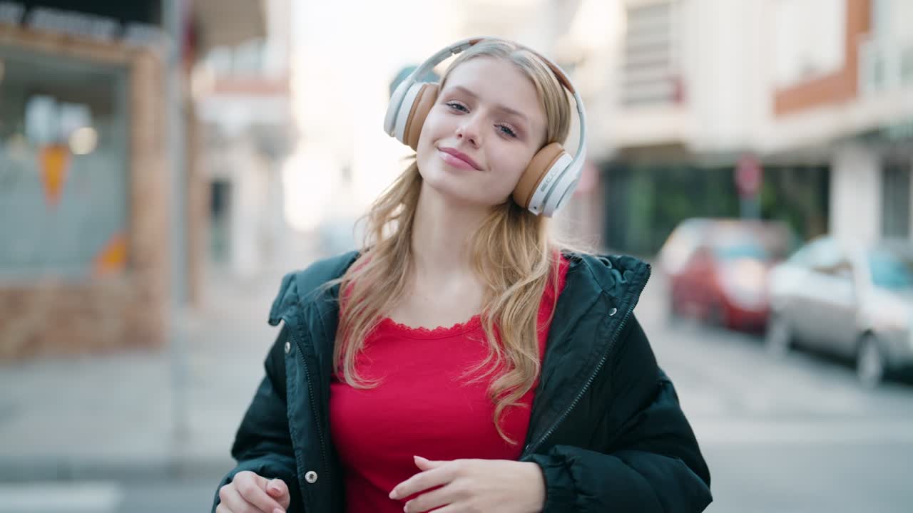 Giovane ragazza bionda che sorride con sicurezza mentre ascolta musica per strada.