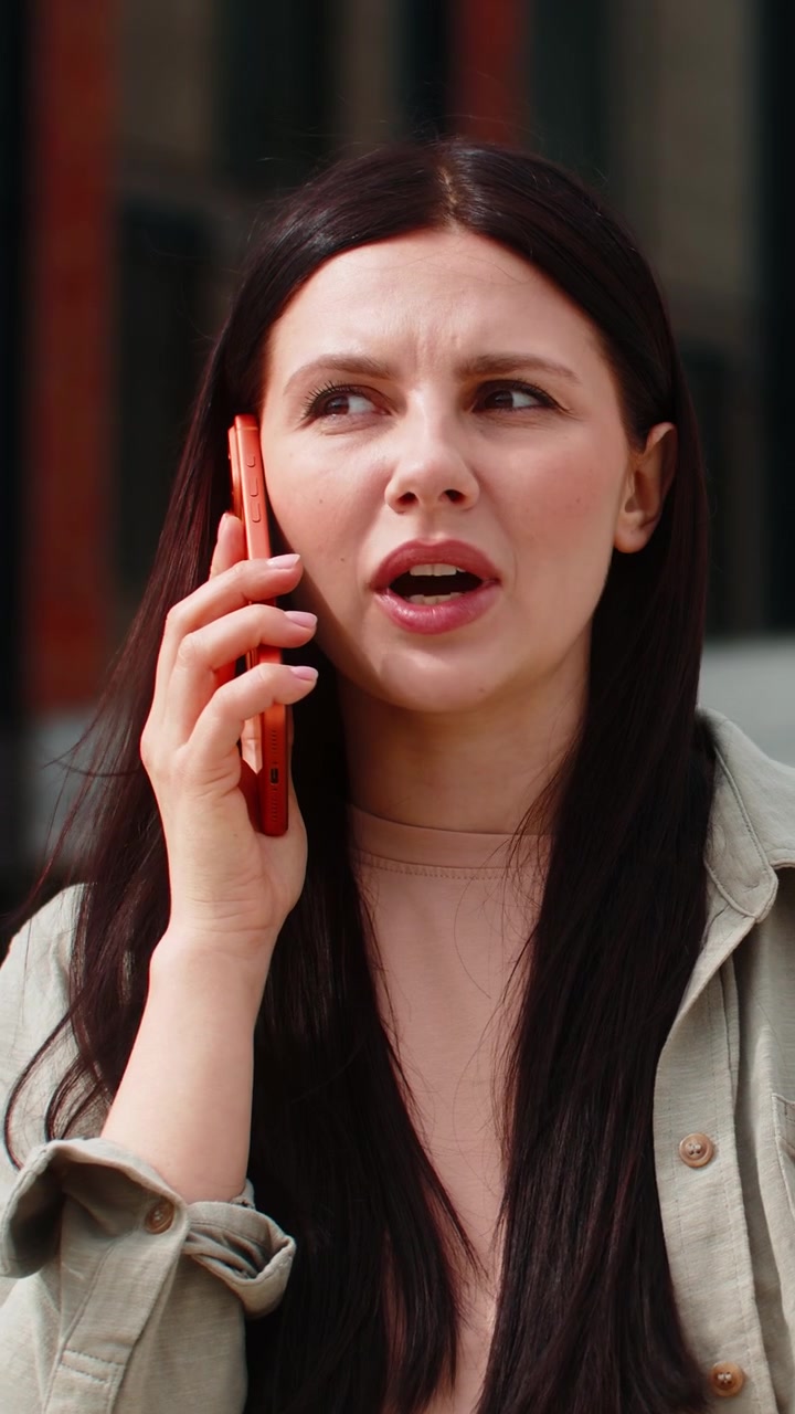 Giovane donna sorridente che parla allo smartphone mentre cammina per strada in città, sentendosi positiva durante una chiamata urbana