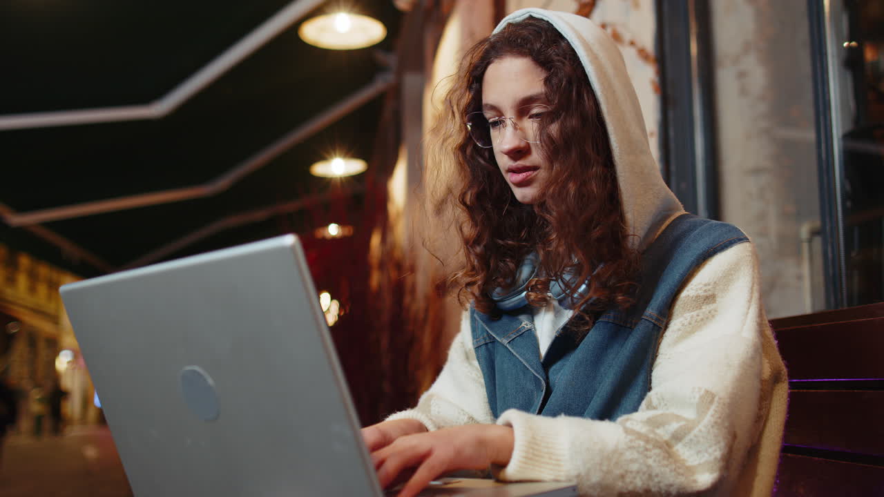 Happy tourist teen girl working online distant job with laptop at city street cafe browsing website
