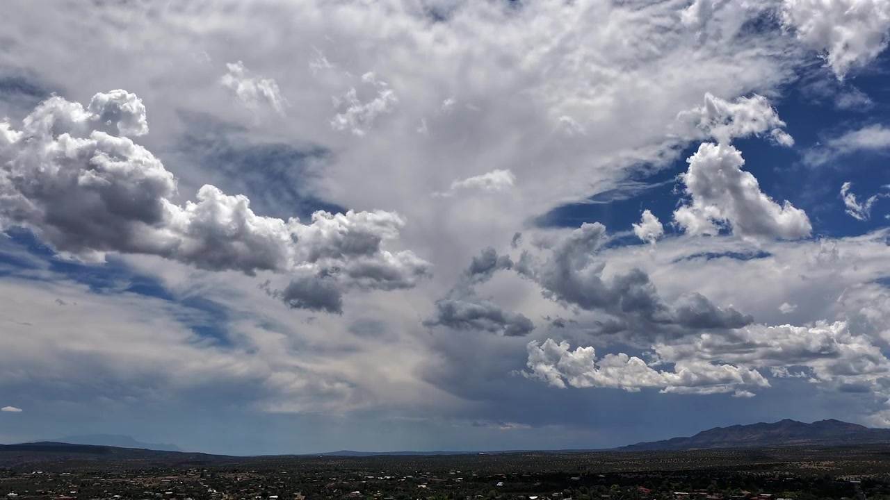 Timelapse 4K UHD con drone che cattura condizioni meteorologiche dinamiche su un insediamento suburbano del sud-ovest. Sorprendenti doppi strati di nuvole testurizzate e frammentate si muovono rapidamente attraverso un cielo blu intenso sopra il paesaggio.