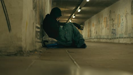 hooded homeless man sits begging in cold dimly lit city urban subway
