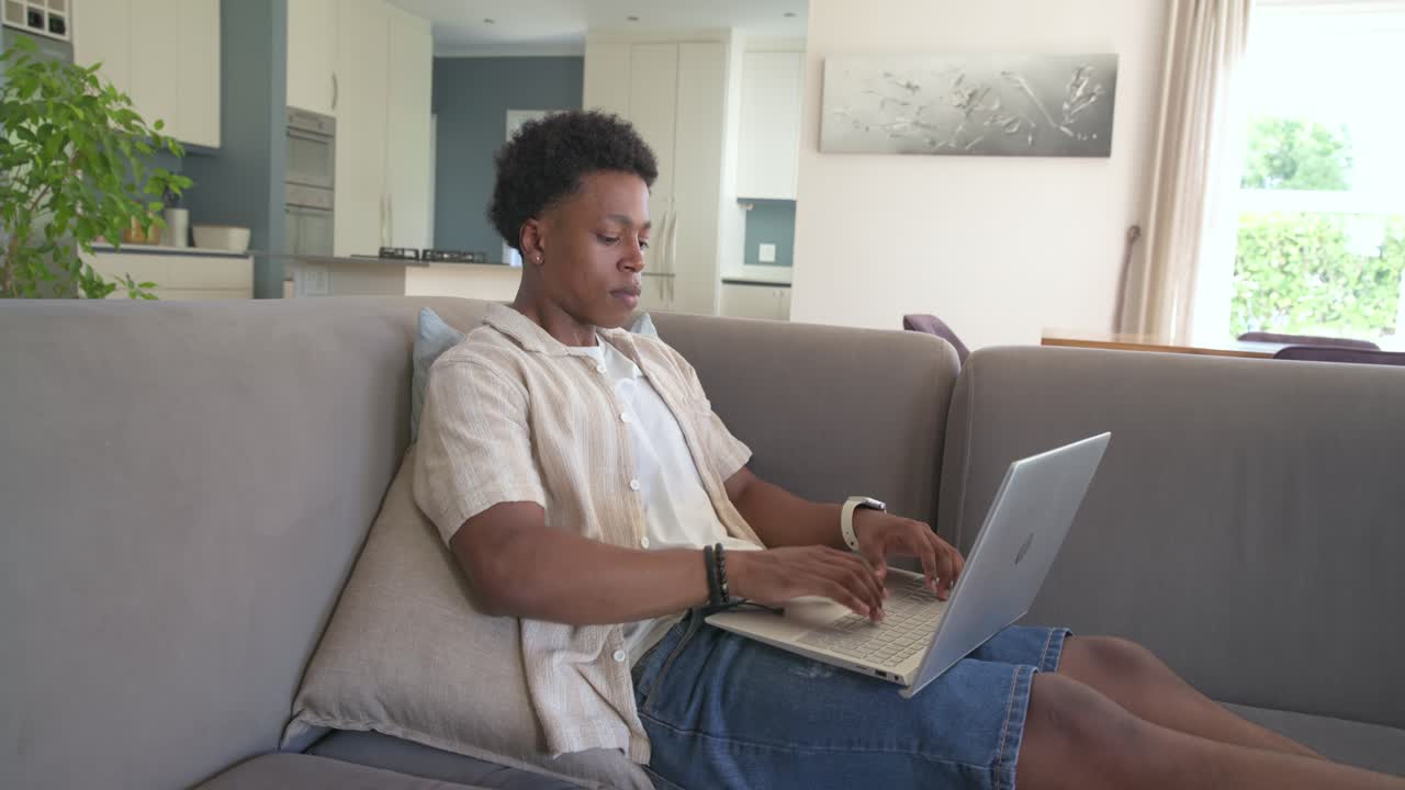African American man pausing from typing on laptop on sofa, closing lid, reclining and resting