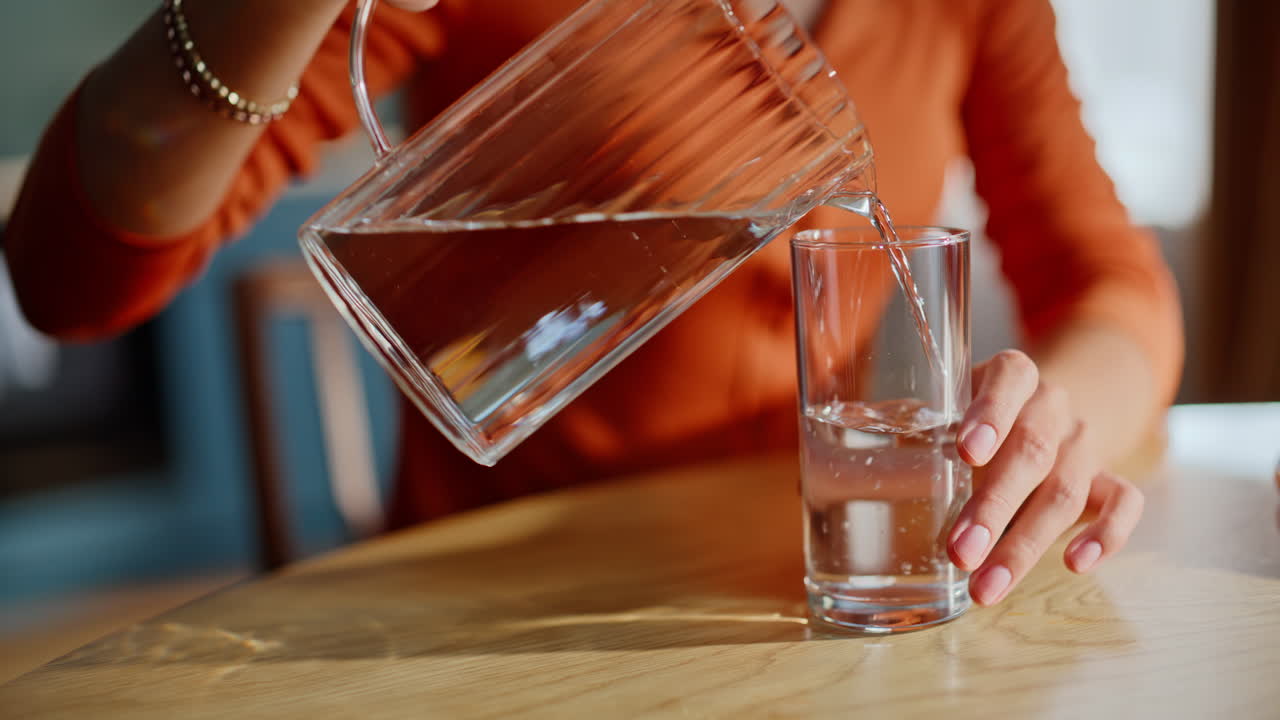 Mani di donna che prendono una brocca d'acqua dal tavolo. Brunetta calma che versa una bevanda fresca