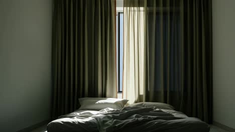 slightly open curtains allowing soft natural light to filter into a dark bedroom, revealing an unmade bed in a tranquil nighttime setting