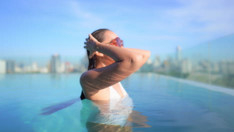 Mit-Einer-Modernen-Skyline-Im-Hintergrund-Eine-Nahaufnahme-Einer-Jungen-Frau-In-Einem-Pool-Auf-Dem-Dach,-Die-Ihr-Nasses-Haar-Glättet