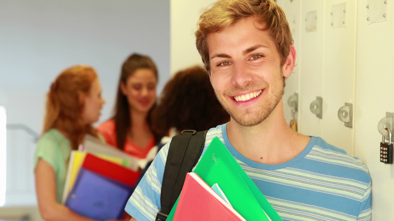 estudiante guapo apoyado en el casillero sonriendo a la cámara