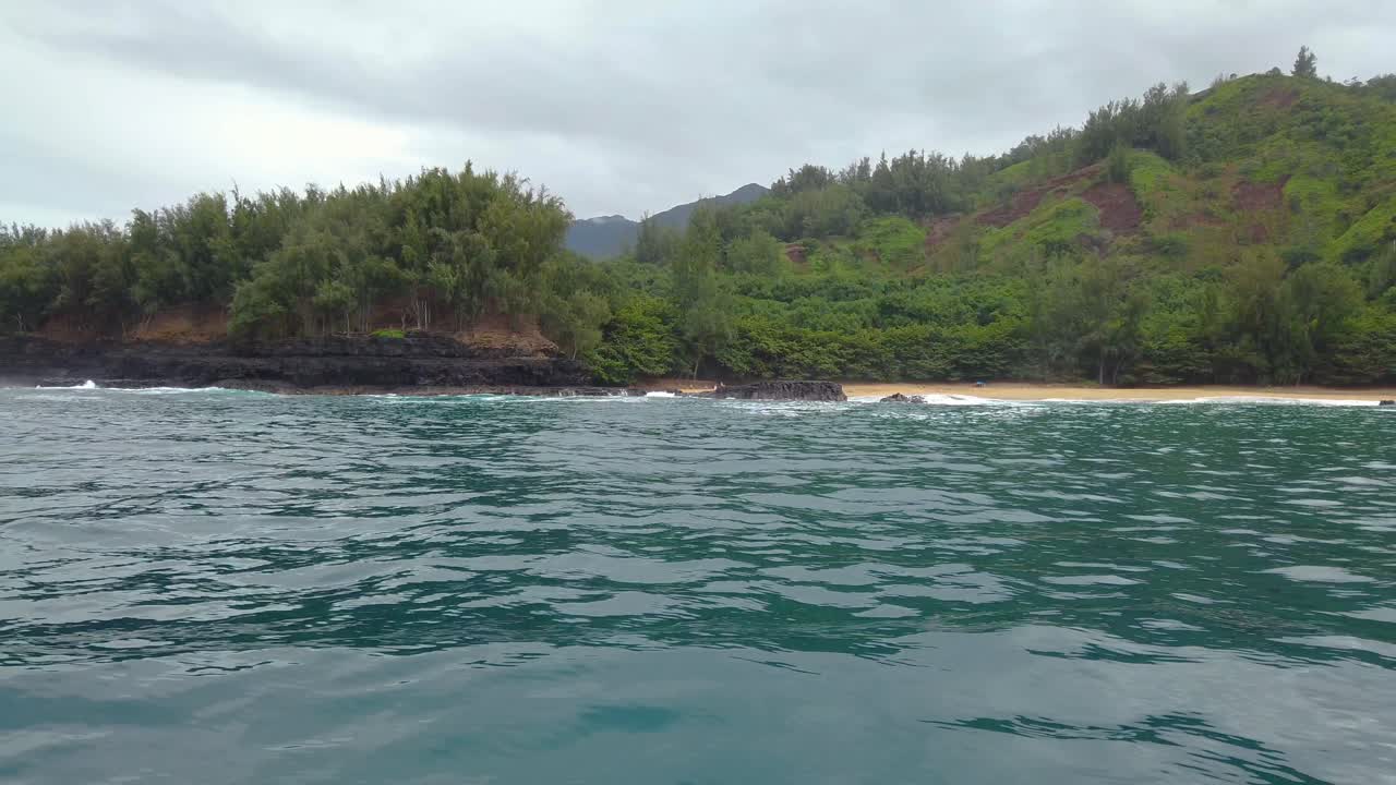 4K Hawaii Kauai Boating on ocean floating right to left from beach to waves crashing on rocky shoreline to reveal more shoreline in cloudy distance